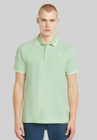 Ljusgrön polo t-shirt med krage och vita ränder, tillverkad av bomull, med en diskret logotyp på vänster bröst, korta ärmar.