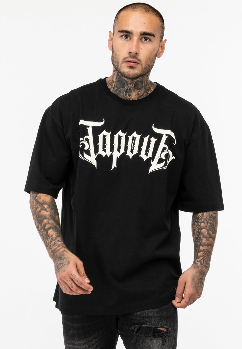 Črna bombažna majica s prenapihnjenim krojem, na sprednji strani z belim Gotskim slogom napisa "Tapout". Kratki rokavi in okrogel izrez.