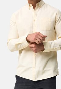 Lysegul langærmet skjorte med knapper har en brystlomme, klassisk krave og en-knaps manchetter, lavet af struktureret stof.