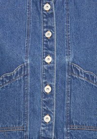 Tissu en denim avec cinq boutons-pression en métal alignés verticalement, surpiqûres orange le long des bords, et poches partiellement visibles des deux côtés.
