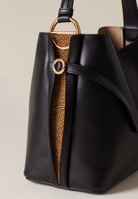 Schwarze Lederhandtasche mit einem goldfarbenen Hardware-Akzent und einem strukturierten braunen Stoffpanel an der Seite, strukturierte Form mit glatter Oberfläche.