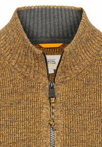 Strickjacke mit Reißverschluss in einem Mix aus warmen Gelb- und Grautönen. Verfügt über eine strukturierte Oberfläche, einen hohen Kragen und einen schwarzen Reißverschluss mit Zugband.