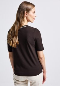 Brown short-sleeve shirt with a rounded neckline and contrasting trim at the collar. Smooth texture, fitted design, and minimalist style.