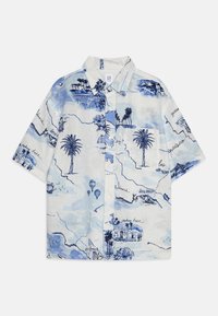 Camicetta a maniche corte in tessuto azzurro chiaro con una stampa a tema viaggio che presenta palme, paesaggi e testo scritto a mano in blu scuro.