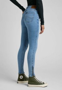 Leggings de mezclilla azul de talle alto con un ajuste slim, que presentan un detalle de cremallera en los tobillos y una etiqueta de cuero en la cintura.