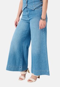 Lichtblauwe wijde denim jeans met een hoge taille, voorzien van een schone afwerking en subtiele stikseldetails, gecombineerd met beige strappy hakken.