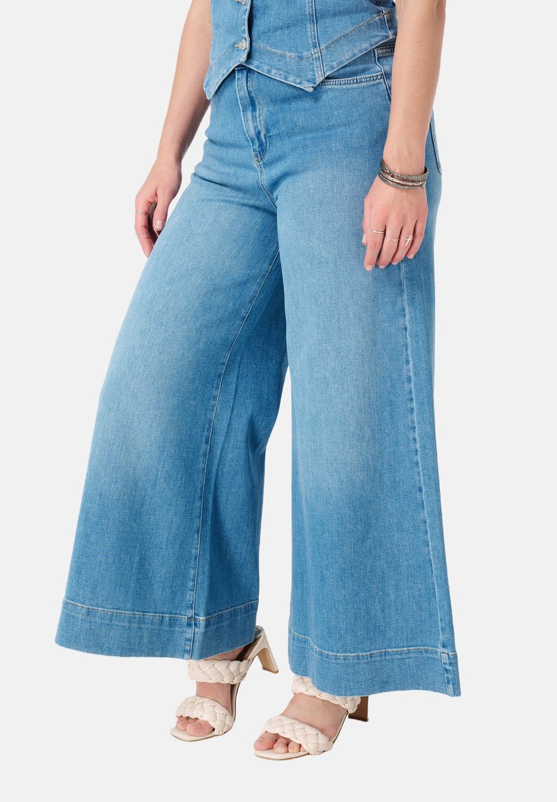Lichtblauwe wijde denim jeans met een hoge taille, voorzien van een schone afwerking en subtiele stikseldetails, gecombineerd met beige strappy hakken.