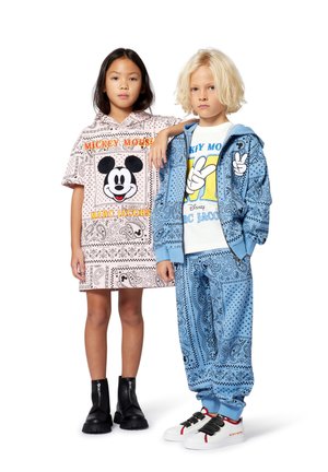 Twee kinderen staan naast elkaar, gekleed in kleding met Mickey Mouse. Links: een roze jurk met patroon. Rechts: een blauwe hoodie en broek met patroon.