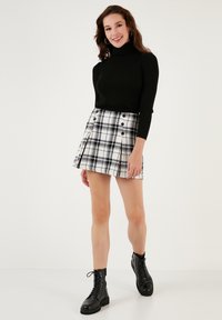 Melnas ribotas turtleneck svārki, apvienoti ar baltu rūtotu plīšo svārku ar melnu akcentu un pogām, valkāti ar melniem šņorējamiem zābakiem.