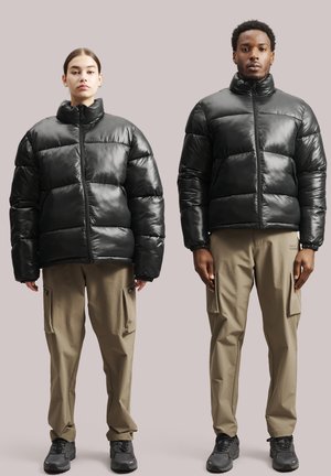 Schwarze Daunenjacken mit glänzender Oberfläche, ausgestattet mit hohen Kragen und durchgehenden Reißverschlüssen, kombiniert mit beigen Cargo-Hosen und schwarzen Schuhen.