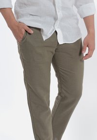 Pantalony z lekkiego materiału w oliwkowym kolorze, z bocznymi kieszeniami, zwężającym się krojem nogawki i gładką teksturą, w połączeniu z białą lnianą koszulą.