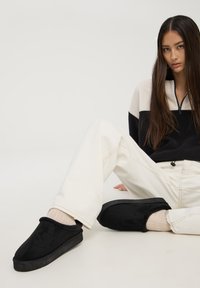 Scarpe slip-on in suede nere con un interno morbido, suola in gomma e forma arrotondata. Indossate con calze color crema e pantaloni chiari.