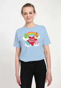 Světle modré bavlněné tričko s potiskem medvídků Care Bears, na kterém je rámeček s duhou, mraky a hvězdami v jasných barvách.