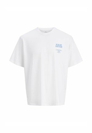 Nastolatek o kręconych włosach, ubrany w biały T-shirt z grafiką, niebieską koszulę w kratę zawiązaną w talii, jeansy z szerokimi nogawkami i brązowe buty, stojący na białym tle.