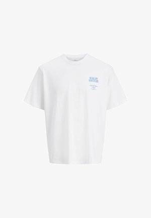 Nastolatek o kręconych włosach, ubrany w biały T-shirt z grafiką, niebieską koszulę w kratę zawiązaną w talii, jeansy z szerokimi nogawkami i brązowe buty, stojący na białym tle.