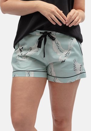Persoon draagt lichtblauwe satijnen shorts met witte zwaanprints en een zwart trekkoord, gecombineerd met een zwarte top.