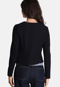 Giacca croppata navy con maniche lunghe, tessuto testurizzato, caratterizzata da un colletto rotondo e dettagli delle cuciture posteriori. Indossata sopra un denim.