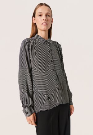 Bluse i sort og hvid stribede med et geometrisk mønster, knaplukning, lange ærmer og krave. Fremstillet af letvægtsstof.