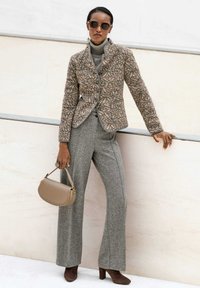Gepersonaliseerde bruine en beige gestructureerde jas, grijze coltrui, grijze slim-fit broek, bruine hakken en een beige handtas.