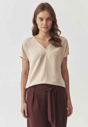 Blouse en satin beige avec un décolleté en V, des manches courtes et une coupe ample, associée à un pantalon taille haute bourgogne foncé avec une ceinture à nouer.