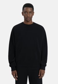 Zwarte sweatshirt met een ronde hals, lange mouwen en geribde manchetten. Gladde textuur, minimalistisch ontwerp, met subtiele branding in de stof.