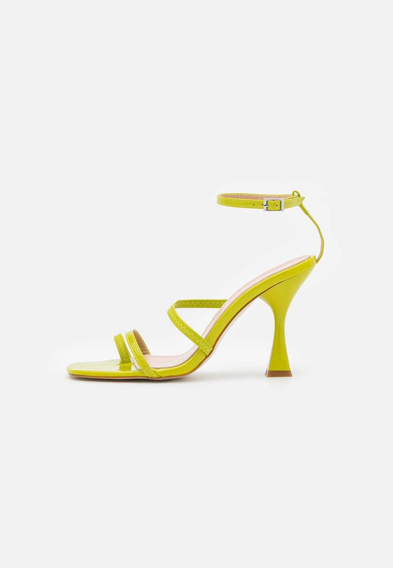 Sandale à talons hauts vert lime brillant avec trois fines lanières et une lanière à boucle à la cheville sur un fond blanc.