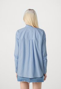 Svetlo modra prugasta srajca z gumbi in dolgimi rokavi, z zadnjim delom in ohlapnim krojem. V kombinaciji z denim krilom.