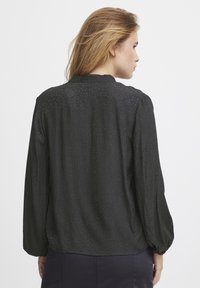 Blusa nera a maniche lunghe con finitura testurizzata, scollatura rotonda e maniche leggermente a sbuffo. Tessuto liscio con un motivo sottile.