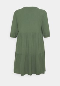 Vihreä, polvenpituinen mekko, jossa on kolme neljänneskättä, pyöreä pääntie ja kerroksellinen rakenne. Valmistettu pehmeästä kankaasta, jossa on sileä pinta.