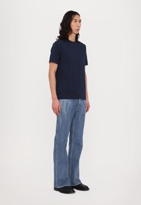 Tricou din bumbac bleumarin, asociat cu blugi evazați de culoare albastru deschis, având o textură netedă și linii curate. Pantofi negri completează ținuta.