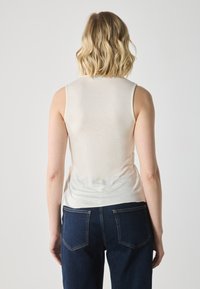 Haut sans manches beige clair avec une texture lisse, encolure ronde et détails froncés sur les côtés, associé à un jean en denim bleu foncé.