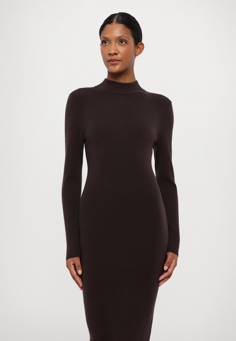 Vestito a maglia marrone con colletto alto e maniche lunghe, forma aderente, texture morbida e design minimalista, esposto su uno sfondo bianco.