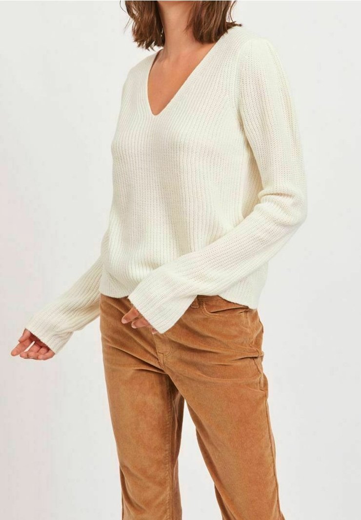Suéter de punto blanco con canalé, con escote en V y mangas largas ajustadas, acompañado de pantalones de pana color beige. Tela texturizada y corte relajado.
