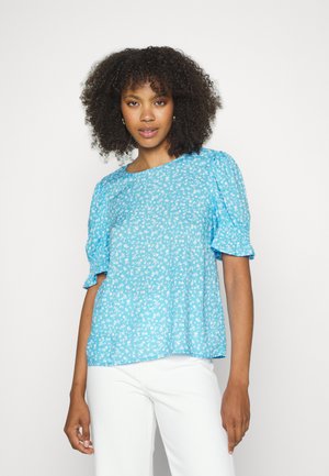 Blusa azul-clara com mangas bufantes curtas, apresentando um padrão floral em branco. O tecido parece suave e leve, com um corte descontraído.