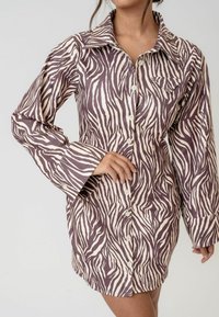 Rochie camasă cu model zebrat în nuanțe de mov și crem. Prezintă un guler, mâneci lungi și închidere cu nasturi pe față.