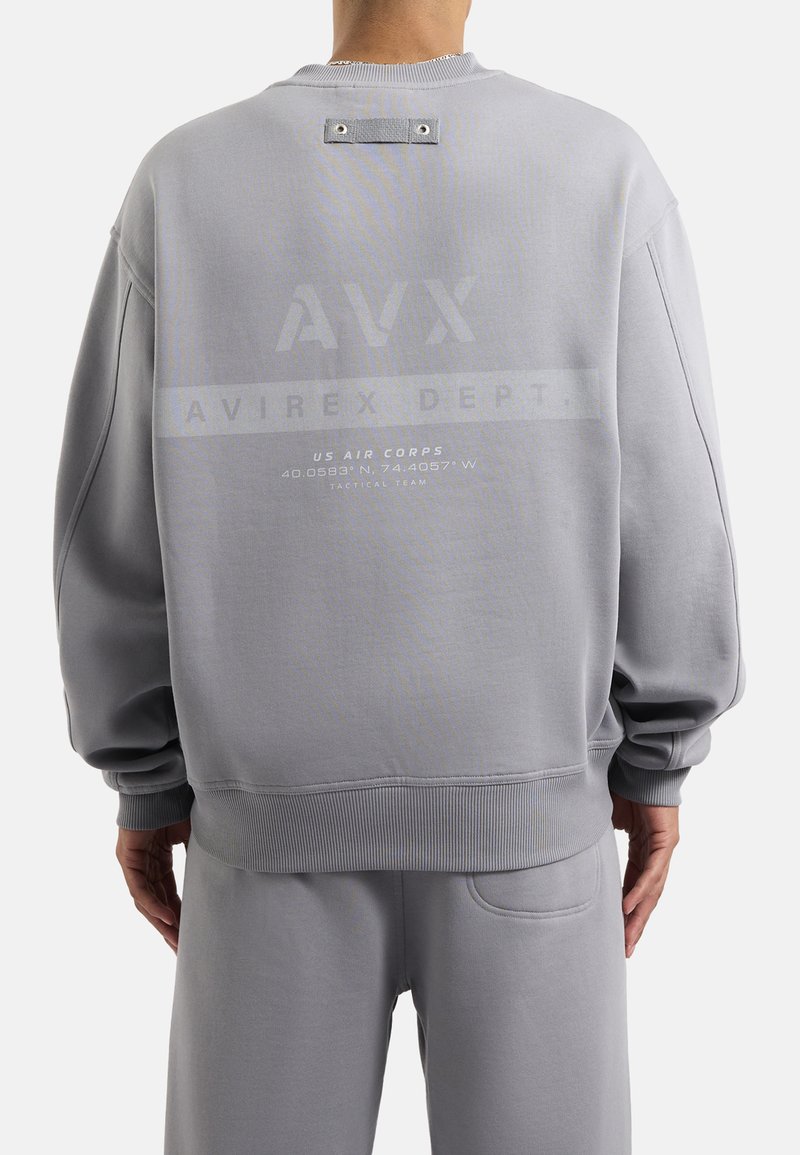 Sweatshirt grigio con scollo a girocollo, spalle cadenti e una grafica stampata sul retro con testo e dettagli in metallo.