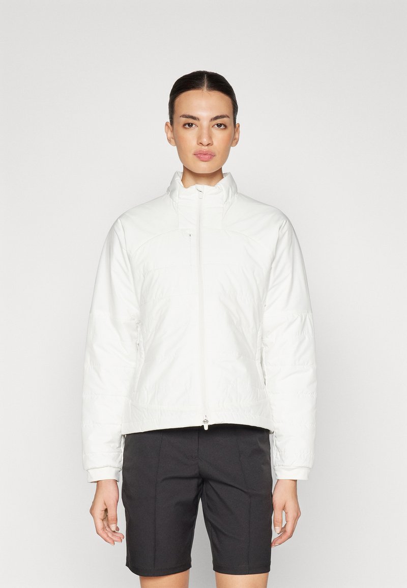 Balta paminkštinta striukė su aukštu apykakle, užtrauktuku ir ilgomis rankovėmis. Lygus paviršius su šiek tiek blizgiu apdailos efektu. Suderinta su tamsiomis šortais.