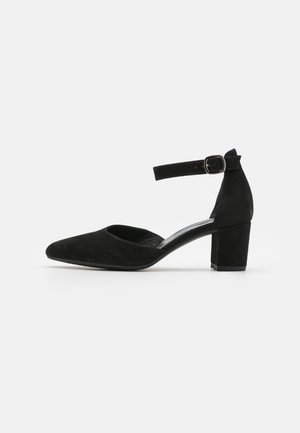 Black suede ankle strap pump with a pointed toe and a block heel. Features a curved cutout on the sides and a metallic buckle for adjustment.