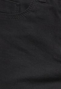 Close-up van zwarte denimstof met zichtbare stiksels en textuur van het voorvak.