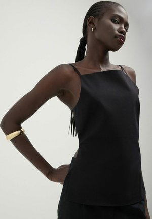 Top nero senza maniche con spalline sottili, dalla texture liscia e taglio dritto. Accentuato da un bracciale d'oro sul braccio sinistro.