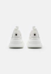 Baskets de sport blanches dotées d'une tige en mesh, d'un talon rembourré, d'une languette d'extraction et d'une semelle texturée pour une meilleure adhérence.