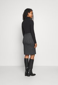Haut à col roulé noir à manches longues associé à une jupe crayon grise longueur genou avec un motif texturé, et des bottes noires montantes.