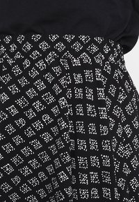 Falda estampada en blanco y negro con un diseño geométrico distintivo de pequeños cuadros y puntos, confeccionada con tela ligera. Cintura elástica.