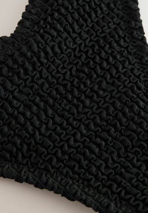 Svart texturerad tyg med insamlad eller smockad detalj, som har ett vågigt mönster och släta kanter. Närbild betonar materialet.