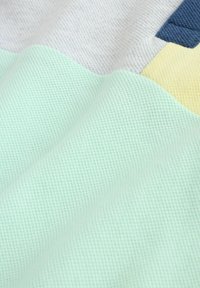 Detailný záber na textíliu s textúrovaným pleteným vzorom v svetlozelenej, bledožltej, bielej a tmavomodrej farbe.