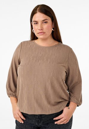 Brown textured blouse with three-quarter sleeves, featuring a round neckline and subtle vertical stripes. Worn with dark jeans.