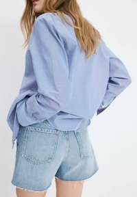 Cămașă cu dungi albastre și albe, cu nasturi și mâneci lungi, asortată cu pantaloni scurți din denim deschis la culoare, cu tivuri desfăcute și buzunare în spate.