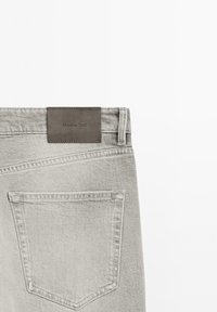 Jean en denim gris clair montrant le haut du dos avec une seule poche et une étiquette en cuir marron cousue avec "Massimo Dutti."