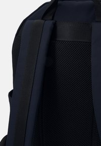 Sezione dello zaino nero con schienale in rete imbottita, spallacci in tessuto nero e parte superiore liscia. Il design enfatizza la traspirabilità e il comfort.