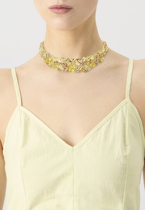 Choker necklace with yellow and clear gemstones, set in a golden metal frame, featuring a floral design. Worn on a bare collarbone.